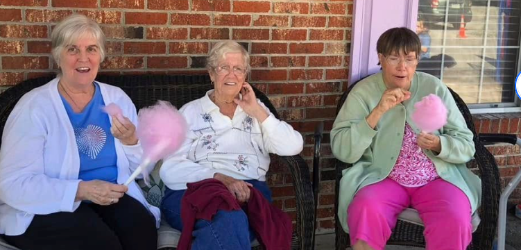 Three residents sitting on the front porch at Lavender Fields, each holding a stick of pink cotton candy