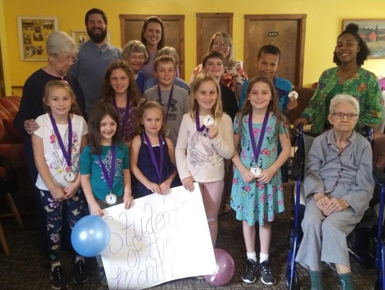 Beverly Grade School Student of the Month award ceremony at Lavender Fields — kids with medals and a handmade sign, residents gathered around them