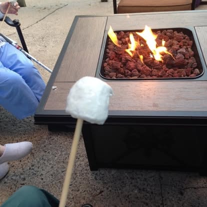 A resident roasting a marshmallow on a stick over the fire pit on the patio