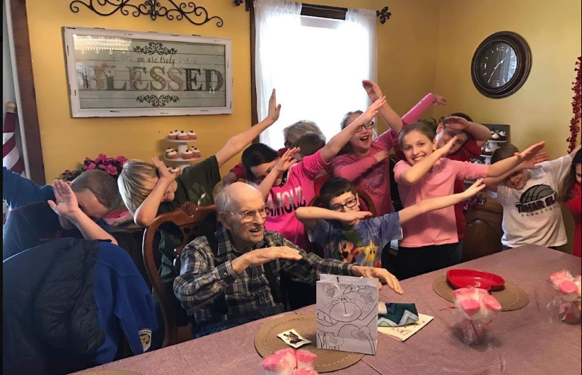 A group of children dabbing and celebrating around a resident at a birthday party in the Lavender Fields dining room