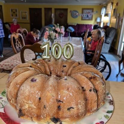 A blueberry bundt cake with gold '100' candles celebrating a resident's 100th birthday at Lavender Fields