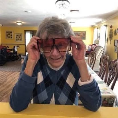 A resident trying on oversized red glasses and grinning in the Lavender Fields dining room